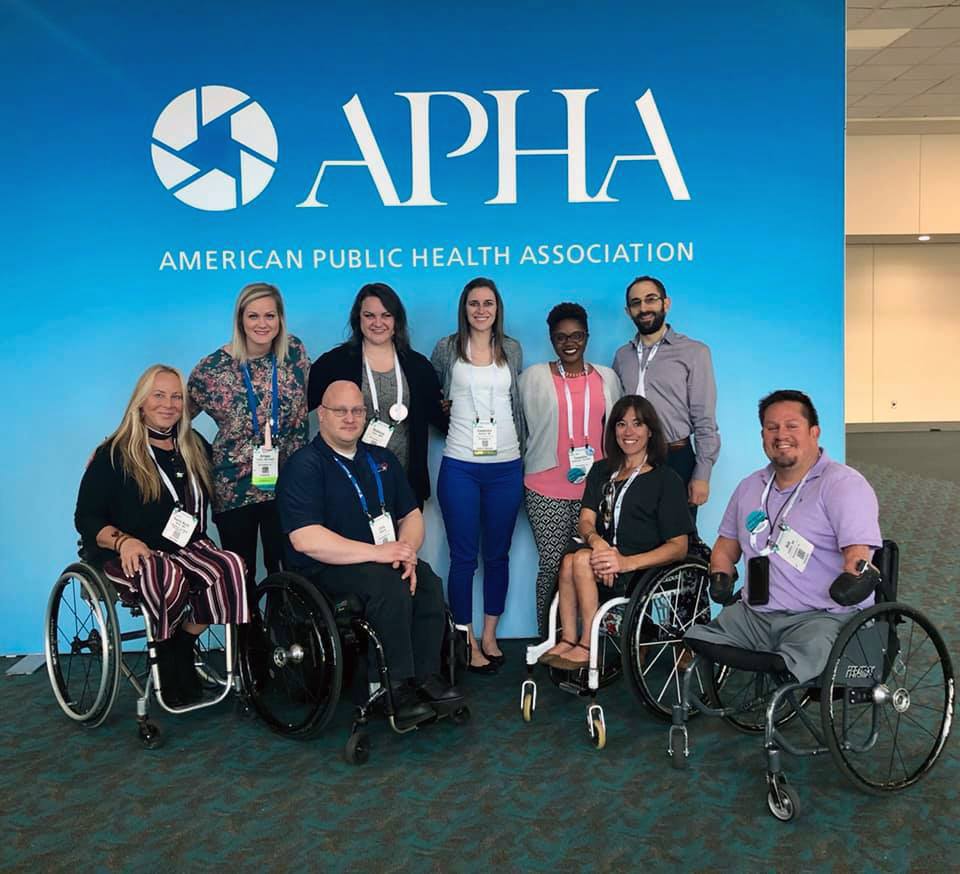 A group of adults pose in front of an American Public Health Association banner.