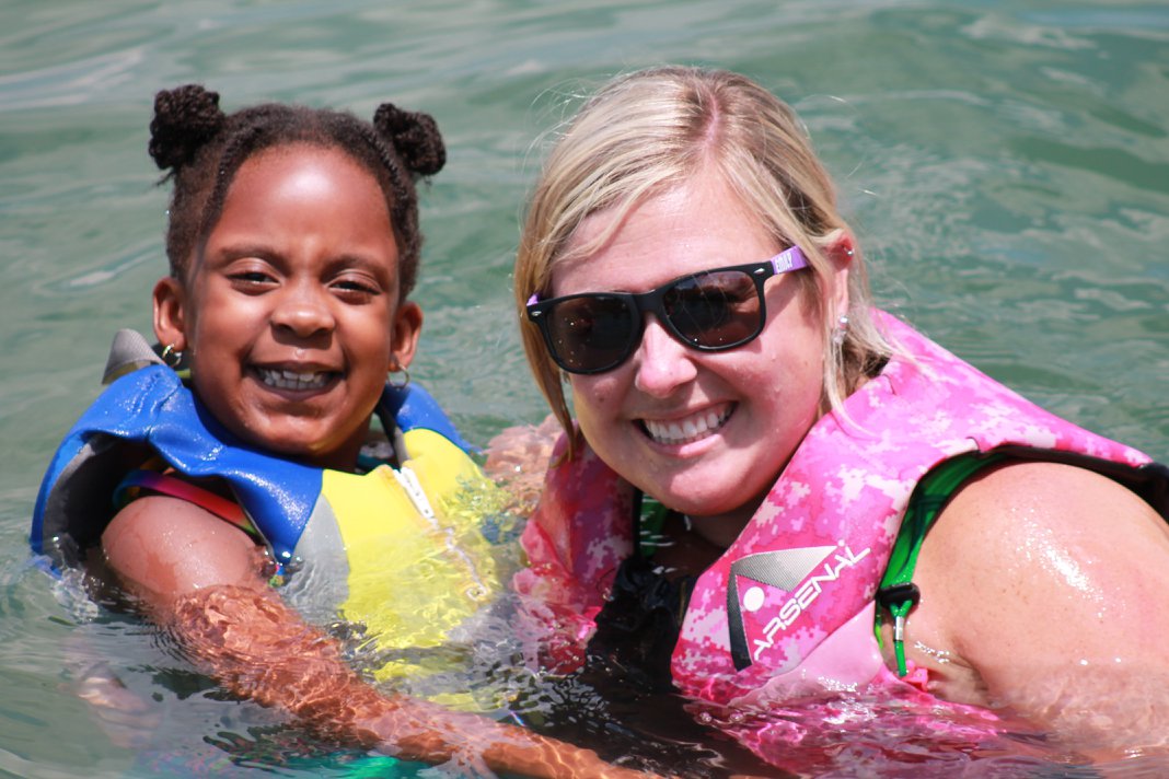 A young girl with black hair and dark skin poses in the water with a woman with blonde hair and light skin.